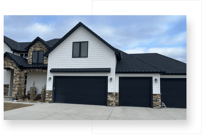 A picture of a house with two black garage doors.